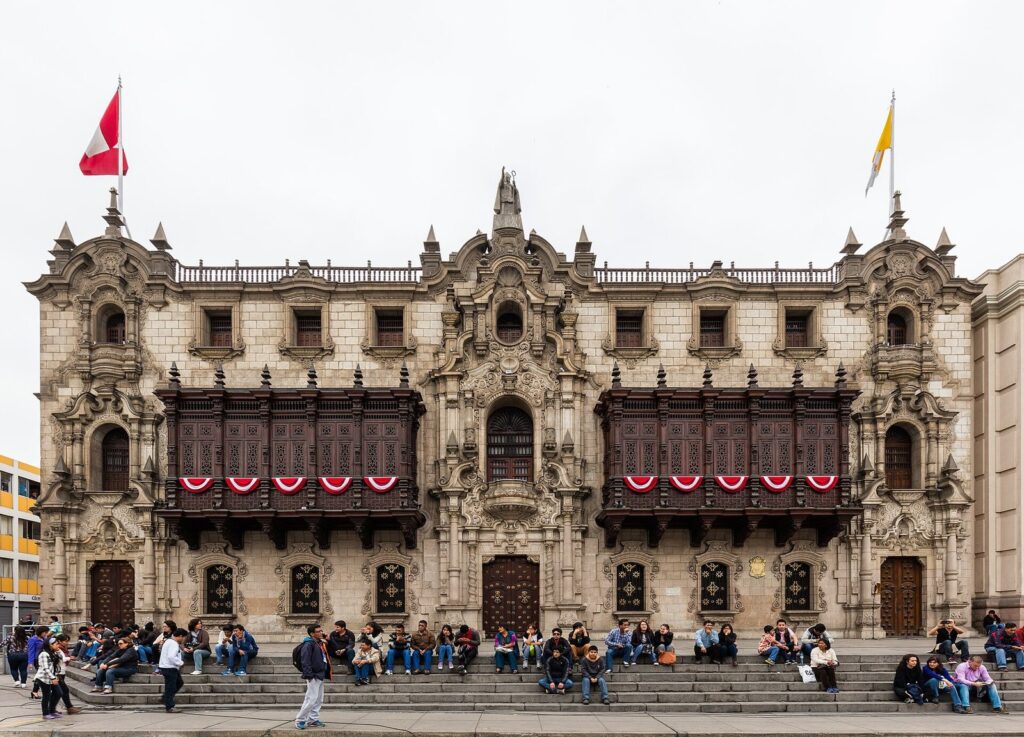 Ornate stone facade of the Archbishop's Palace on Lima's Plaza Mayor with two long enclosed wooden balconies carved in dark wood
