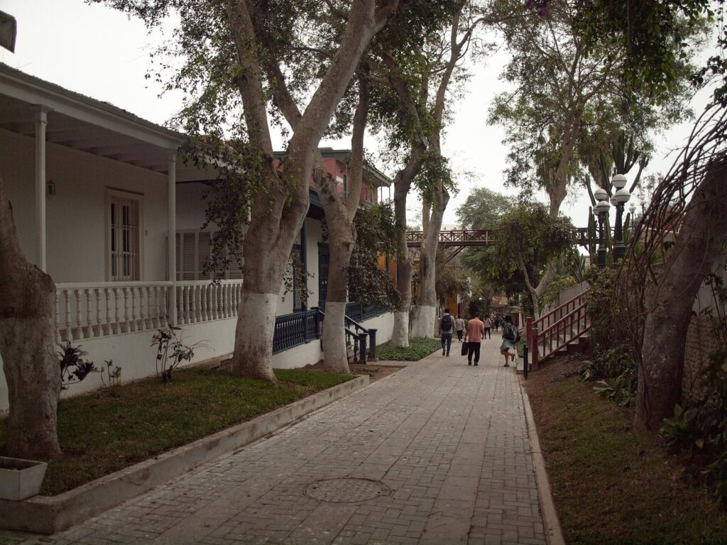 Tree-shaded stone path of the Bajada de los Baños in Barranco, Lima, lined with old white houses with wooden porches and railings