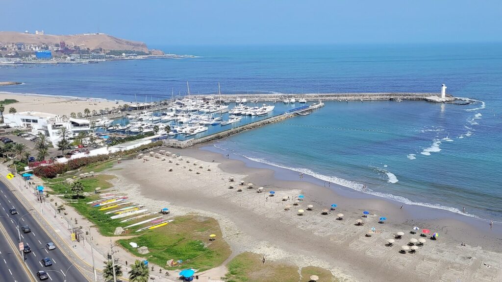 Beach with sun umbrellas, a yacht marina and the Costa Verde highway at Barranco in Lima, Peru, with the Morro Solar headland across the bay