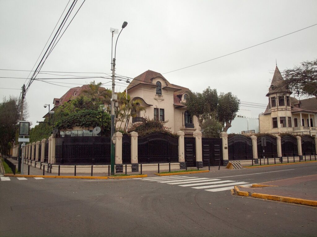 Republican-era mansions with turrets and tiled roofs behind iron fences on a street corner in Barranco, Lima, under a gray sky