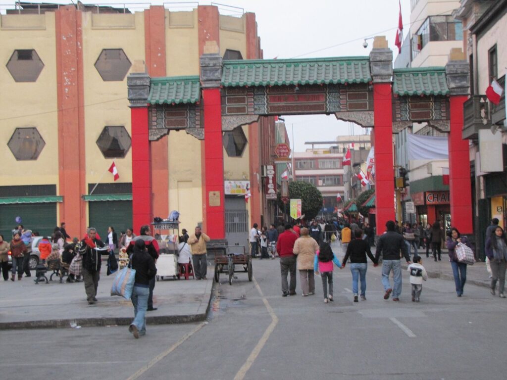 Red Chinese-style gateway arch over the pedestrian Calle Capón in Lima's Chinatown, with people walking beneath it
