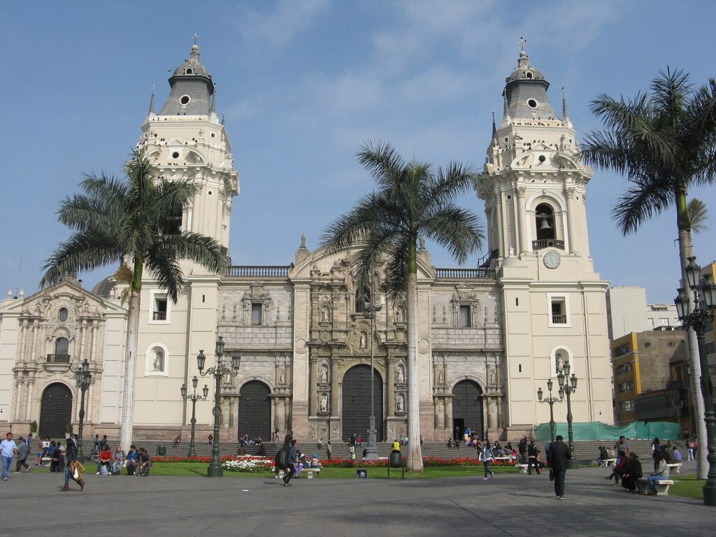 Twin white bell towers and carved stone facade of the Cathedral of Lima behind palm trees on the Plaza Mayor