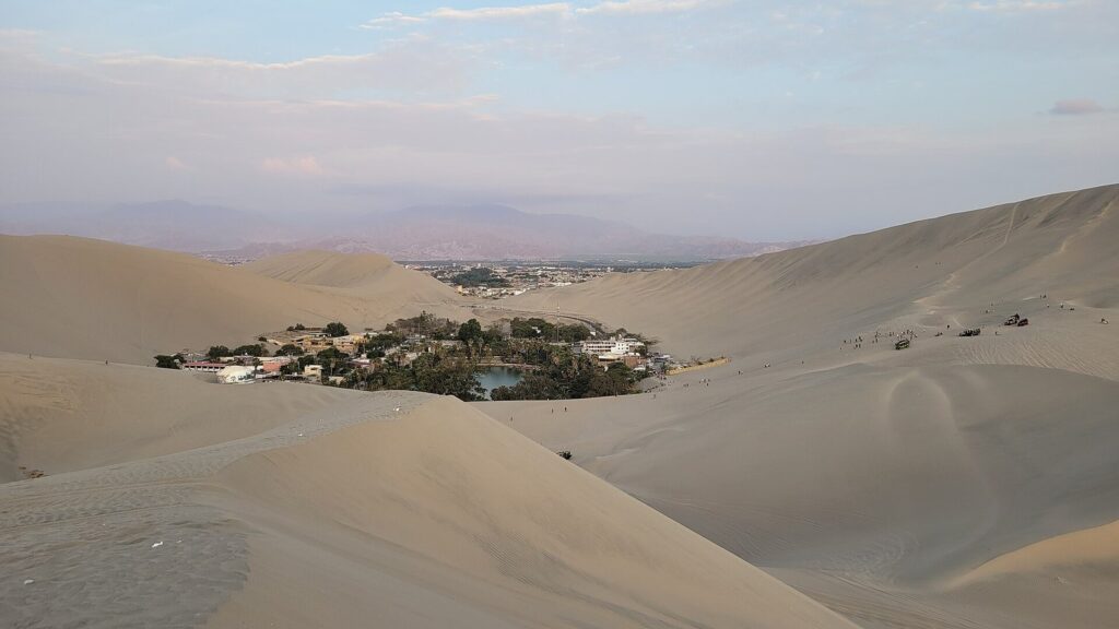 The Huacachina oasis, a green lagoon ringed by palms and buildings among tall sand dunes near Ica, Peru