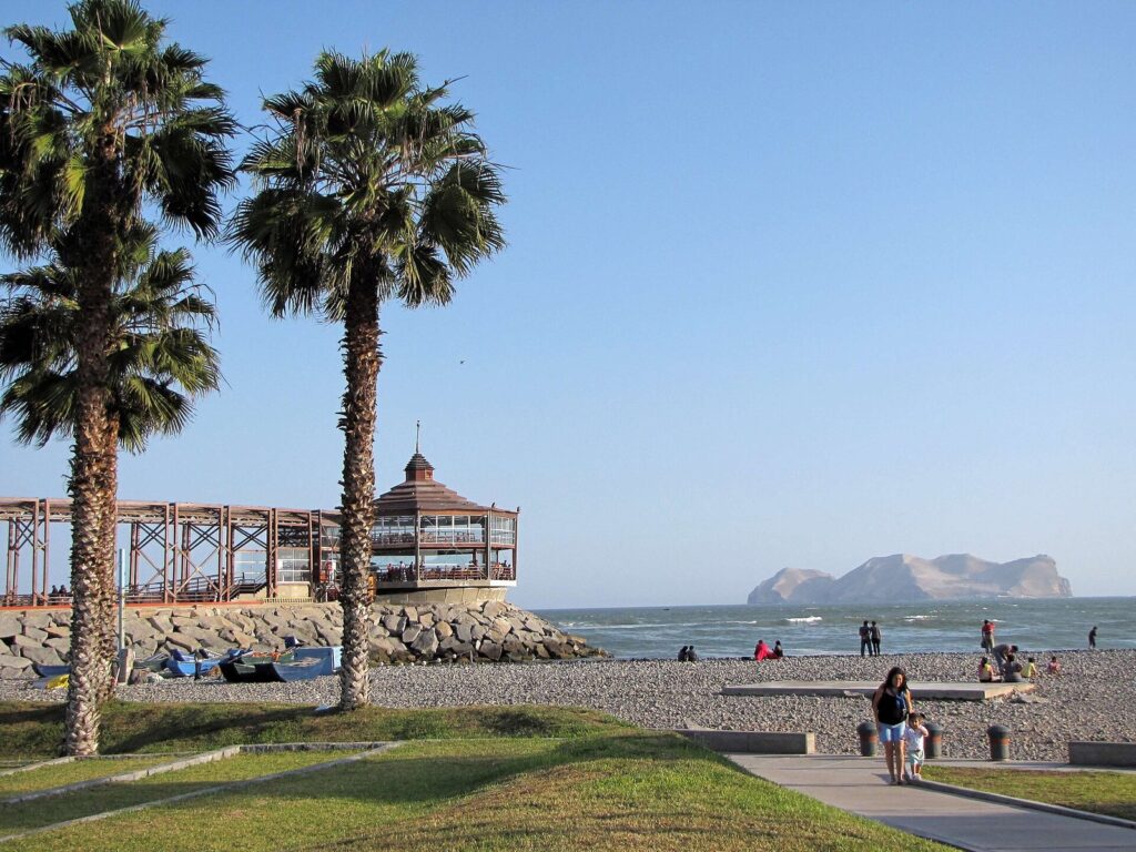 Palm trees, a pebble beach and a wooden pier pavilion on the seafront at La Punta, Callao