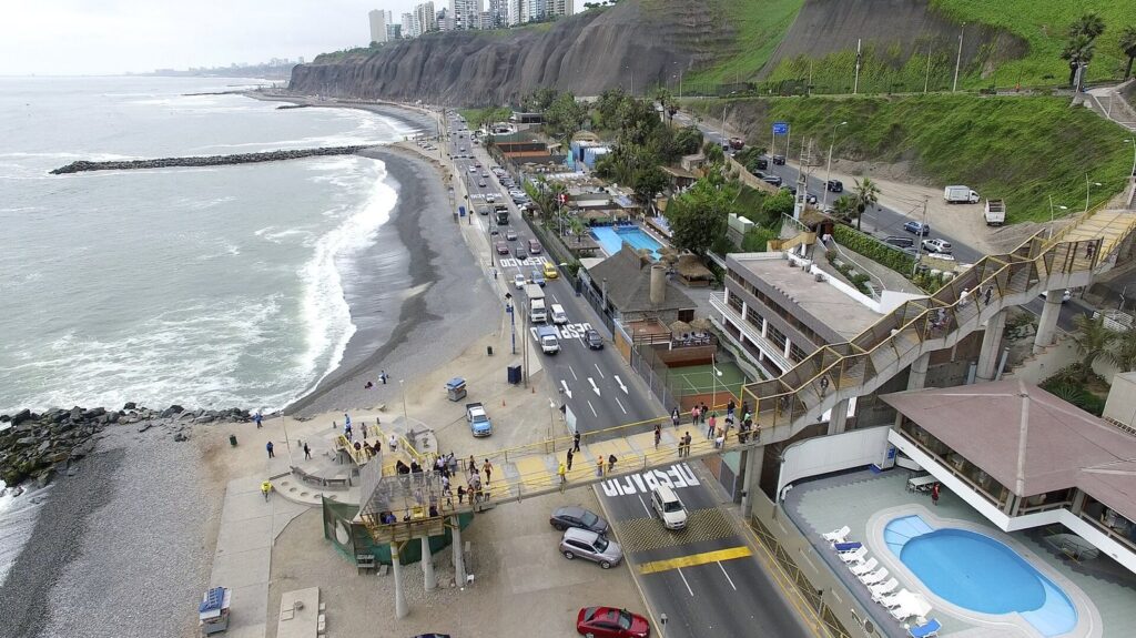 Aerial view of the Costa Verde below the Miraflores cliffs in Lima, Peru, with a pebble beach, a breakwater, the coastal highway and a footbridge up to the clifftop