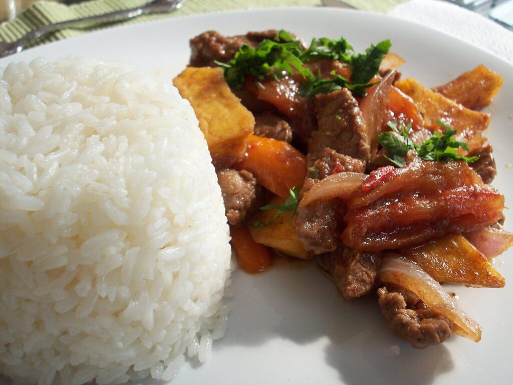 Plate of Peruvian lomo saltado with strips of beef, red onion, tomato and fried potatoes beside a mound of white rice