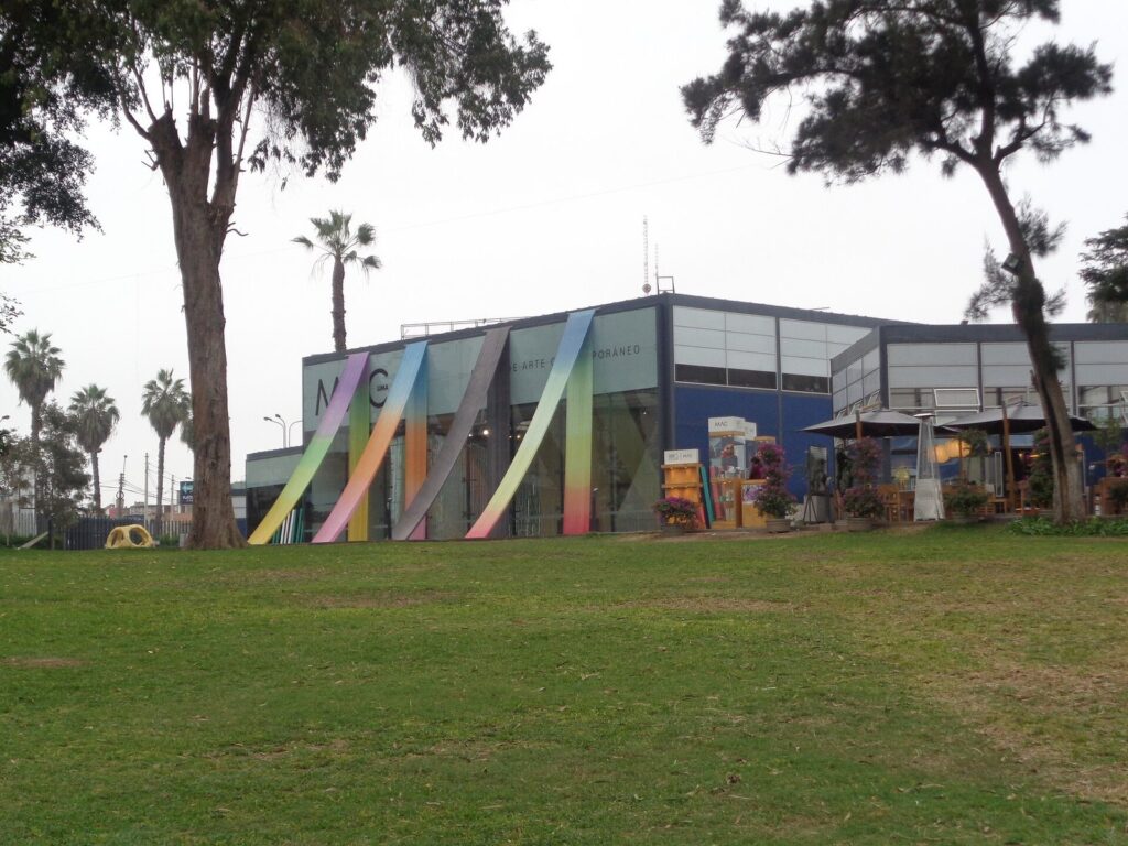 Low modern building of the Museo de Arte Contemporáneo de Lima in Barranco behind a lawn, with a colorful arched sculpture at the entrance