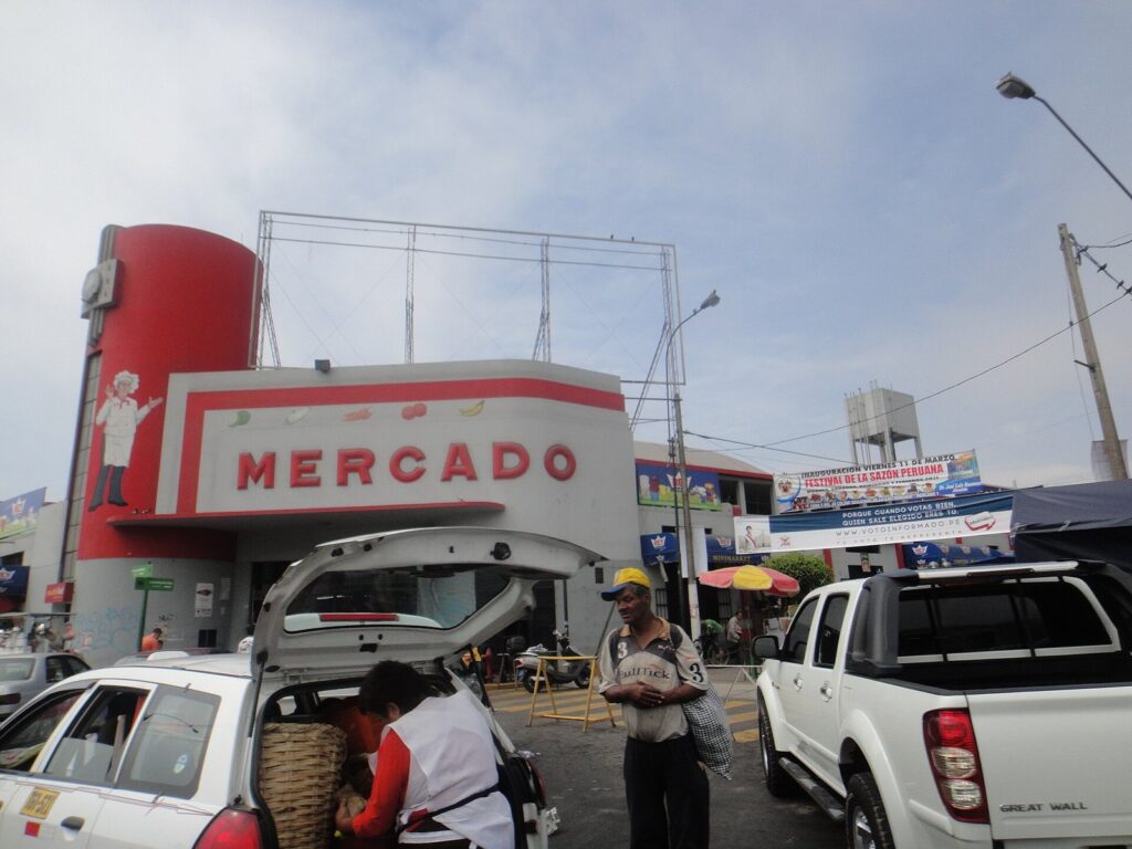 Entrance of the Mercado N° 1 de Surquillo in Lima, Peru, with a red and white sign reading Mercado and cars parked outside