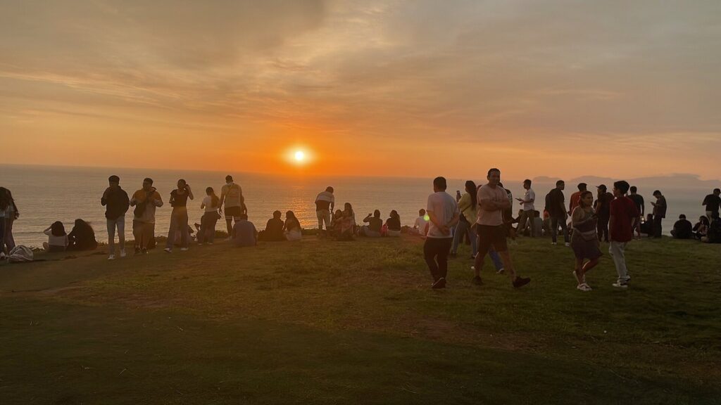 Crowd on a clifftop park in Miraflores, Lima, watching the orange sun set over the Pacific on a summer evening