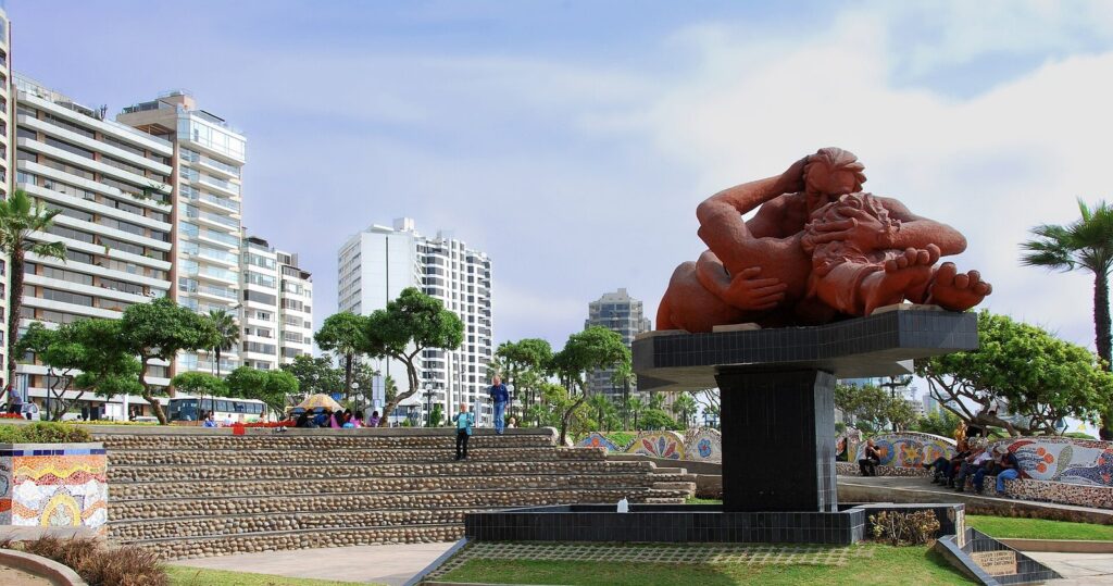 Víctor Delfín's El Beso sculpture of an embracing couple in Parque del Amor, Miraflores, Lima, with high-rise towers and palm trees under a blue sky
