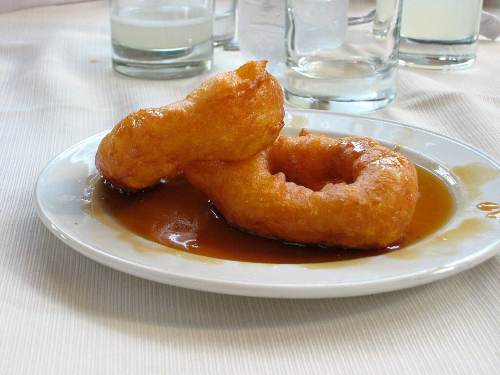 Two picarones, fried rings of dough, in dark syrup on a white plate in Lima, Peru