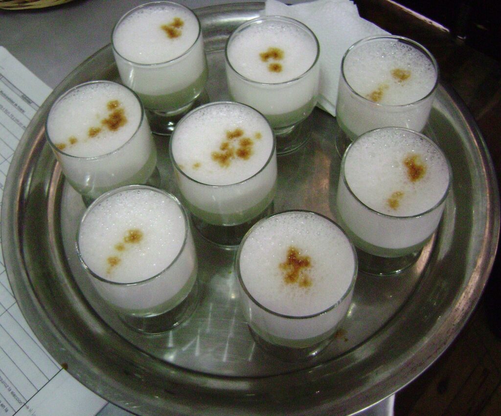 Tray of frothy pisco sour cocktails topped with drops of bitters in short glasses