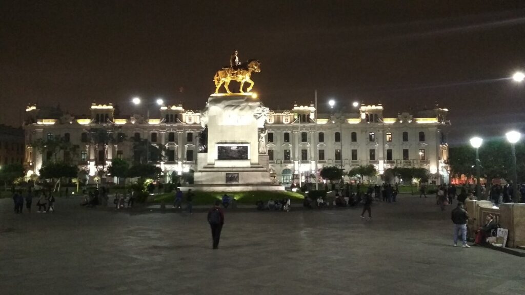 Plaza San Martín in Lima's historic center at night, with the floodlit equestrian monument and white colonnaded buildings behind it