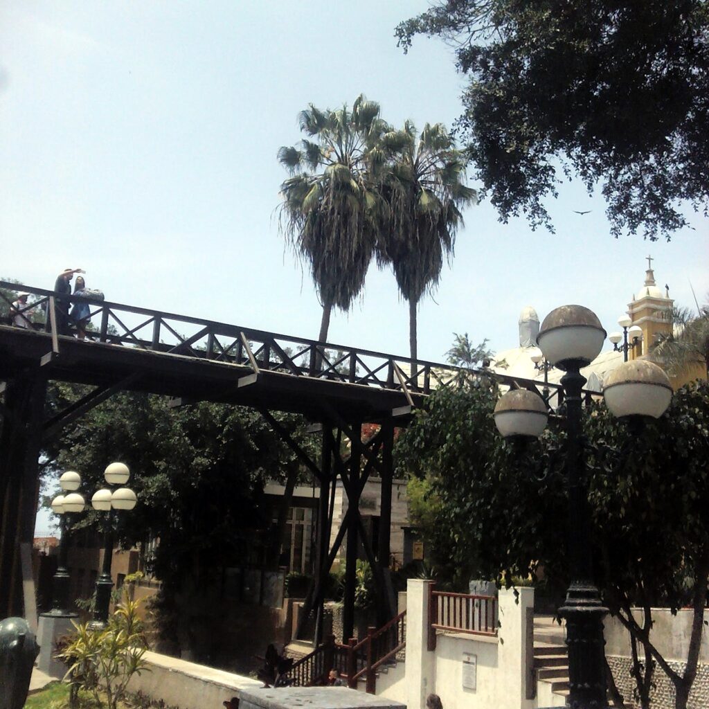 The wooden Puente de los Suspiros footbridge in Barranco, Lima, framed by palm trees and a church tower