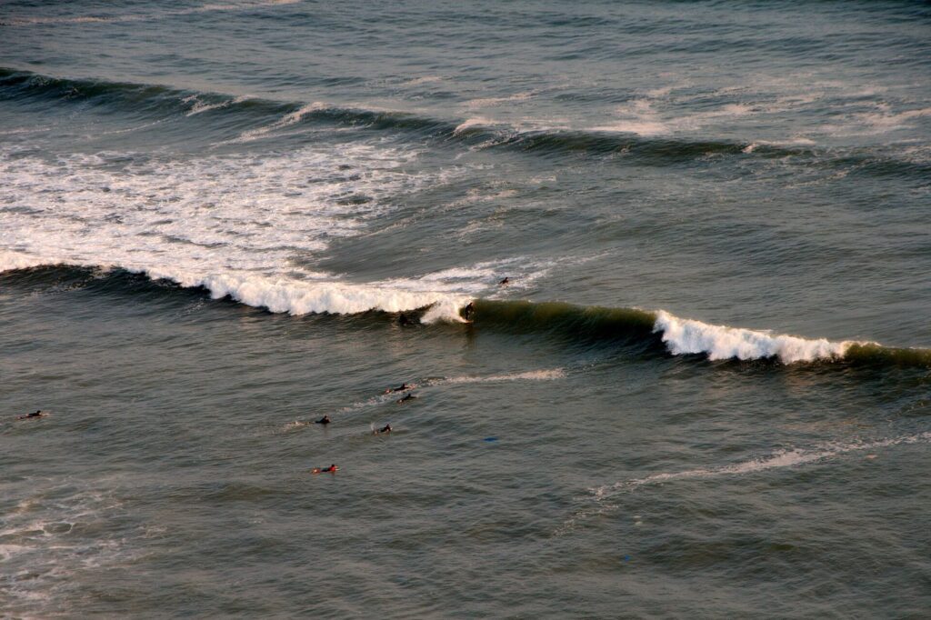 Surfers waiting for waves off the Miraflores beaches in Lima, with long lines of swell breaking toward a pebble shore below the cliffs